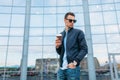 The guy in stylish sunglasses, a man walks around the city and drinking coffee from a paper Cup, a handsome guy walks around and r Royalty Free Stock Photo