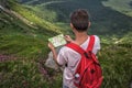 Man with red backpack lost in mountains, holding trip map, paves tourist route Royalty Free Stock Photo