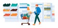 Guy with trolley in the supermarket . Showcases, refrigerator, shelves of goods, wooden boxes of vegetables and fruits. Royalty Free Stock Photo