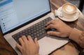 A guy is typing in a chat on laptop and coffee cup and saucer kept aside on wooden table