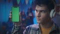 The guy in white headphones shows a smartphone with a green screen. Close up of a guy with a smartphone on a blurred Royalty Free Stock Photo