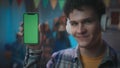 The guy in white headphones shows a smartphone with a green screen. Close up of a guy with a smartphone on a blurred Royalty Free Stock Photo