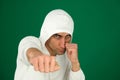 a guy in a white hoodie on a green chromakey background hits the camera with his fist a stern angry look defense attack