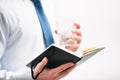 A guy in a white shirt and blue tie on a white background. A man holds a glass with a cocktail and in his second hand is notepad. Royalty Free Stock Photo