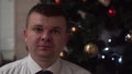 Guy in white shirt, tie shows heart with his hands. Christmas tree background