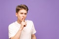 Guy in a white T-shirt put his finger to the lips and shows a sign of silence, isolated on a purple background. Man says: Shh, Royalty Free Stock Photo