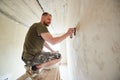 Guy at wooden stand is puttying the walls indoors small room in the daytime. Royalty Free Stock Photo