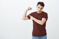 Guy working out but still weak. Portrait of gloomy displeased handsome guy in red t-shirt lifting arm and showing biceps