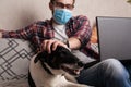 The guy works at home on freelance with his pet. The guy interacts with a dog on the couch with a medical mask Royalty Free Stock Photo