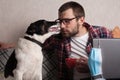 The guy works at home on freelance with his pet. The guy interacts with a dog on the couch with a medical mask Royalty Free Stock Photo