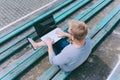 The guy works at a laptop on a bench outdoors against a background of grass.