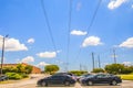 Large industrial power poles and lines with a cloudy blue sky over cars