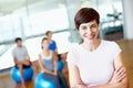 Gym instructor smiling. Portrait of beautiful female gym trainer with people practicing yoga in background. Royalty Free Stock Photo