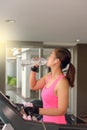 Gym woman working out drinking water by moonwalker fitness machines.