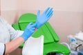 Gynecologist puts on gloves on the background of a gynecological chair. Medical examination