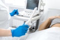 A gynecologist sets up an ultrasound machine to diagnose a patient who is lying on a couch. A transvaginal ultrasound scanner of