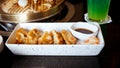 Gyoza served on a white platter with brown sauce and chopped veggies. A BBQ may be seen in the backdrop