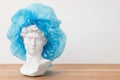 Gypsum copy of David`s head in surgical cap. Michelangelo`s David plaster bust, ancient sculpture, statue on wooden Royalty Free Stock Photo