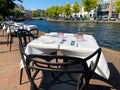 View on neatly set tables for dinner with empty chairs at riverside of Spaarne river in the evening sun