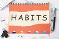 HABITS word is written on a sheet in a cage lying on a notebook on the table next to stationery
