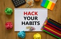 Hack your habits symbol. White note with words Hack your habits on wooden table, colored paper, colored pencils, paper clips,