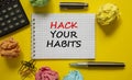 Hack your habits symbol. White note with words Hack your habits on yellow table, colored paper, colored pencils, paper clips,