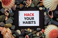 Hack your habits symbol. Words `Hack your habits` on white note, black background. Sea stones and seashells. Business, psycholog