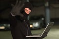 Hacker in balaclava gesturing and using laptop Royalty Free Stock Photo