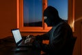 Hacker in Balaclava Typing on Laptop in a Dark Room, hacking concept Royalty Free Stock Photo