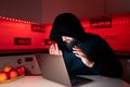 A hacker in a black hoodie with a hood on his head is sitting at a laptop with his palms spread in front of the computer Royalty Free Stock Photo