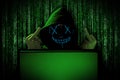 Hacker with blue glowing mask behind notebook laptop in front of green source binary code background internet cyber hack attack Royalty Free Stock Photo