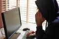 A hacker in a hooded sweatshirt with a hidden face typing on a computer keyboard and talking on a mobile phone. Royalty Free Stock Photo