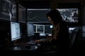 Hacker dressed in a hoodie, sitting in a dark room surrounded by monitors, coding malicious software. Ai generated