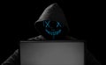 Hacker with glowing mask behind notebook laptop in front of isolated black background internet cyber hack attack concept