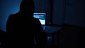 Hacker hacks programs. Computer scammer. Programmers working intently on laptop, typing in dark room with shadowy
