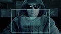 Hacker in hood and dark glasses sits in front of virtual screen and writes code for password decryption. Hacker get