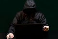 A hacker in a hood, without a face, on a black background sits at a laptop and enters data from a stolen credit card Royalty Free Stock Photo