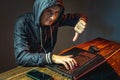 Hacker in a hood with a phone is typing on a laptop keyboard in a dark room. Cybercrime fraud and identity theft Royalty Free Stock Photo