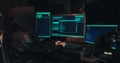 Hacker in a hood sits in front of computer screens and hacks databases Royalty Free Stock Photo