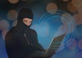 Hacker with hood using a laptop in front of digital background Royalty Free Stock Photo