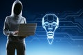 Hacker in hoodie using laptop with abstract robot head in the shape of light bulb on blue background with lines. Artificial Royalty Free Stock Photo