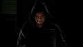 Hacker in hoodie using laptop and looking into camera with evil eyes, malware