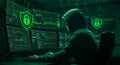 Hacker in hoodie working on computer with multiple screens displaying code and security icons. Cybersecurity and data breach Royalty Free Stock Photo