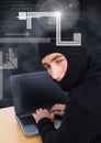 Hacker looking the lens and using a laptop in front of black background