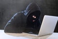 Hacker man in black hood and mask with computer laptop hacking system in digital intruder cyber crime concept