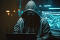 Hacker in a mask and hood looks at the laptop screen. Hacking and malware concept.