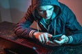 Hacker with phone is typing on a laptop keyboard in a dark room under a neon light. Cybercrime fraud and identity theft Royalty Free Stock Photo