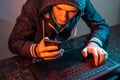 Hacker with phone is typing on a laptop keyboard in a dark room under a neon light. Cybercrime fraud and identity theft Royalty Free Stock Photo