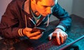 Hacker with phone is typing on a laptop keyboard in a dark room under a neon light. Cybercrime fraud and identity theft Royalty Free Stock Photo