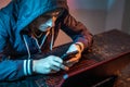 Hacker with phone is typing on a laptop keyboard in a dark room under a neon light. Cybercrime fraud and identity theft Royalty Free Stock Photo